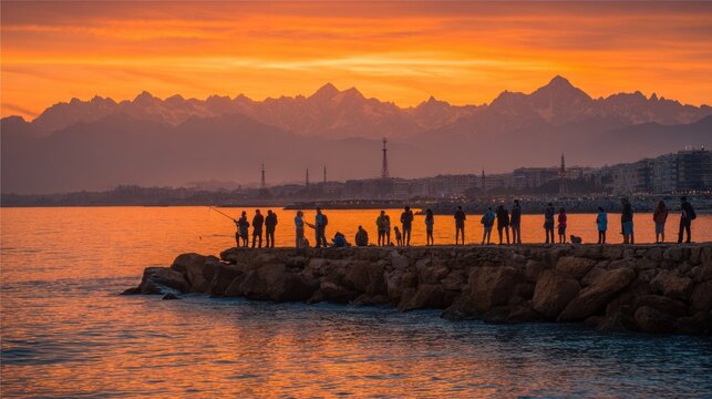 Silhouetted figures enjoy sunset fishing along a stone jetty with distant mountains and a cityscape visible.