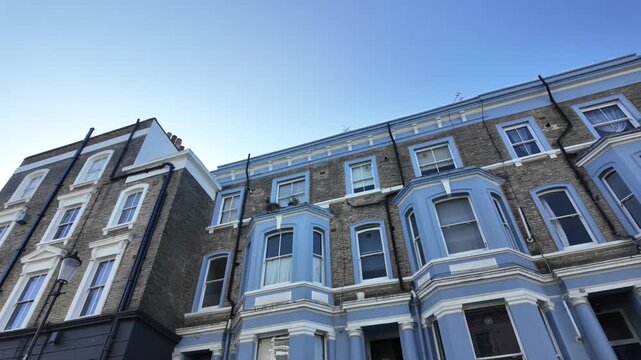 Low angle view tracking shot of colorful victorian terraced houses in notting hill, london, against a clear blue sky, capturing the traditional british architecture