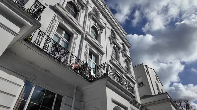 Low angle view revealing the white victorian architecture facade of a residential building in london, with clouds gracefully moving across the beautiful blue sky