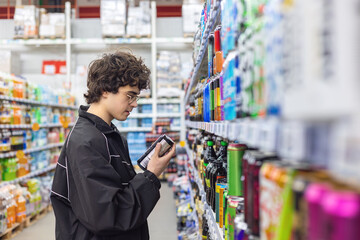 Naklejka premium Teenage boy choosing canned beverages in supermarket and reading product label. Energy drink consumption, sugar intake, caffeine habits and health awareness for adolescents concept.