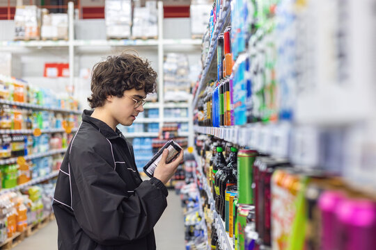 Teenage boy choosing canned beverages in supermarket and reading product label. Energy drink consumption, sugar intake, caffeine habits and health awareness for adolescents concept.