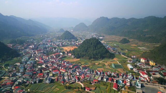 Aerial view of mountain town surrounded by limestone hills and rice fields in Ha Giang, Vietnam. Scenic rural landscape with traditional villages and dramatic northern Vietnam nature.