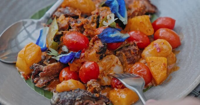 Roasted duck curry plated with pineapple and cherry tomatoes, served on banana leaf plate, Thai Kaeng Phed Ped Yang garnished with blue pea flowers, commercial food photography
