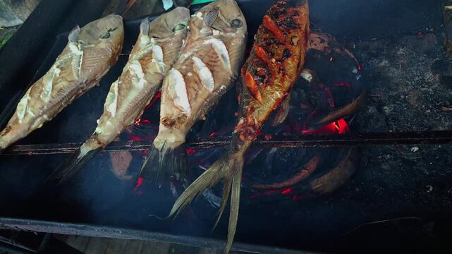 Savory whole fish perfectly seasoned and slow-cooked over glowing charcoal on an outdoor barbecue, promising a delicious and aromatic grilled seafood feast for an unforgettable dining experience