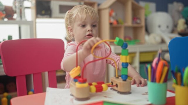 Little blonde girl reaches with hand to slide beads on a wooden bead maze in playroom; concentration learning.