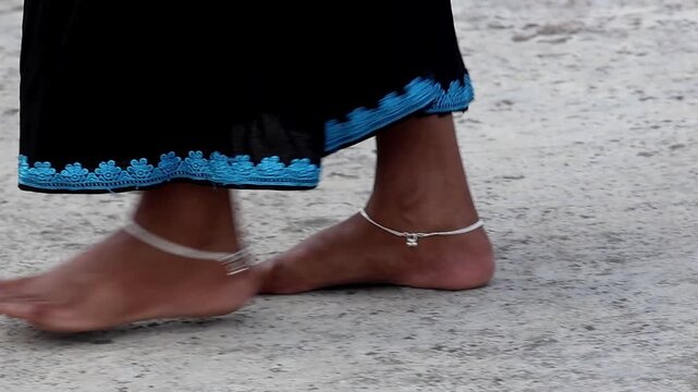 Close-up of female feet with ethnic silver nupur anklets walking on a stone rooftop surface. Traditional jewelry details and barefoot movement for cultural or fashion content.