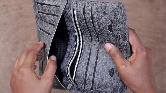 Female hand opening a stylish grey leather wallet showing no money. Concept of financial struggle, lack of cash, and economic crisis. Detailed shot of an empty woman's purse for debt and poverty.