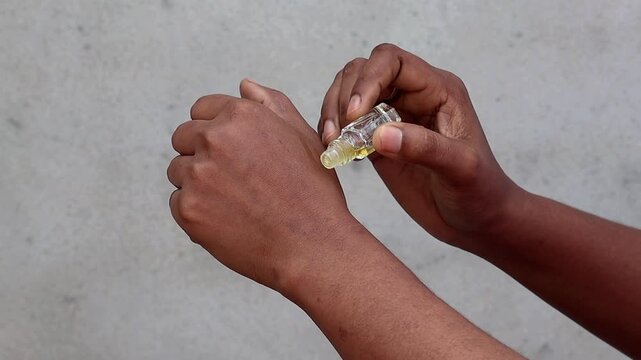 Close-up of a female hand applying traditional aromatic luxury attar perfume oil on her wrist using a glass roll-on bottle. Concept for Islamic culture, halal fragrance, grooming, and herbal beauty.