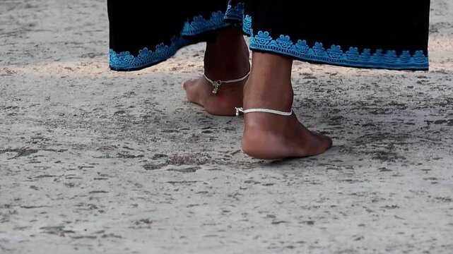 Close-up of a South Asian woman walking barefoot on a concrete rooftop, wearing traditional silver anklets or nupur jewelry. Elegant footsteps of a girl in payal on a sunlit urban floor.