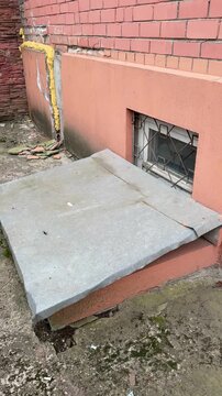 Basement window with metal cover, stucco wall and grated vent, stainless sheet protecting cellar well from rain, concrete ledge