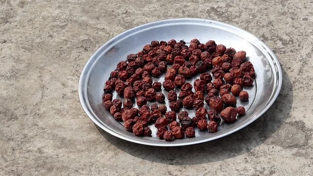 Close-up of dried jujube fruits or red dates spread on a metal plate under the sun. This shot represents traditional sun-drying food preservation methods and organic South Asian fruit snacks.