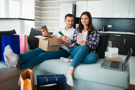 A young married couple buys things online. Around them lies a lot of goods in paper packaging, boxes and bags.