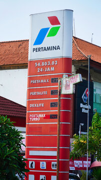 Pertamina gas station in Bali. Gasoline prices in 2024.Gas station sign displays fuel prices in Indonesia during the day near a busy street with shops and trees in the background