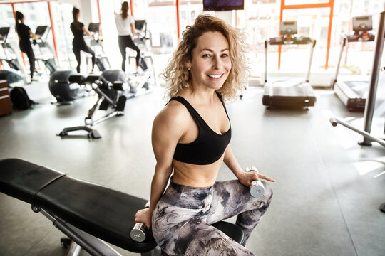 A woman is sitting on a training apparatus. She is looking at the camera and smiling