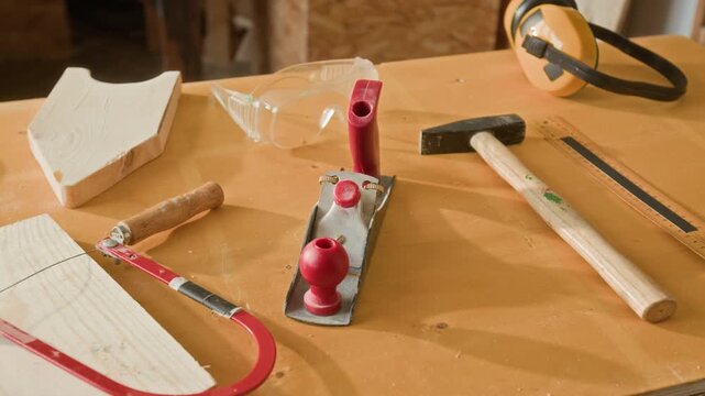 Close-up shot of woodworking tools including hammer, hand plane, coping saw and safety glasses on wooden workbench