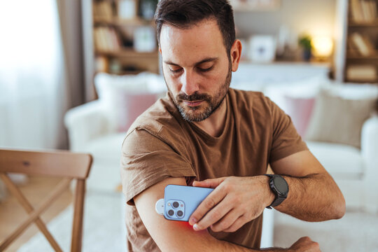Man Scanning Wearable Health Sensor On Arm With Smartphone At Home For Remote Monitoring