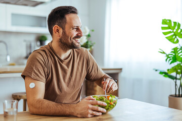 Smiling Man Eating Healthy Salad at Home With Continuous Glucose Monitor Patch on Arm
