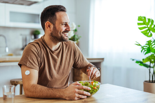 Smiling Man Eating Healthy Salad at Home With Continuous Glucose Monitor Patch on Arm