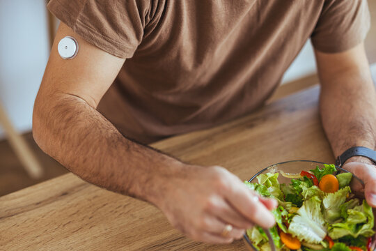 Man With Continuous Glucose Monitor Eating Healthy Salad At Kitchen Table Managing Diabetes Routine
