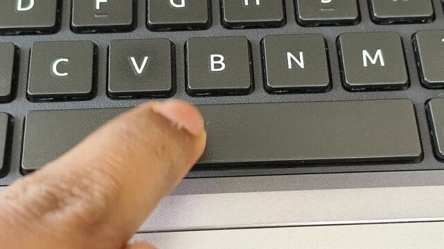 Close up of finger pressing or rage click laptop spacebar button on keyboard. Angry and frustrated employee or user repeated rapid tap on non responsive, slow, hang or frozen computer device concept.