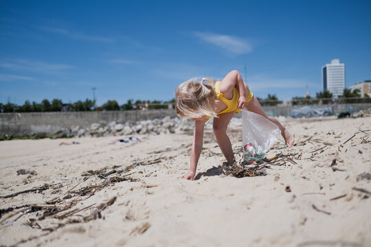Little girl volunteer collecting plastic waste and garbage in bag on the sandy city beach