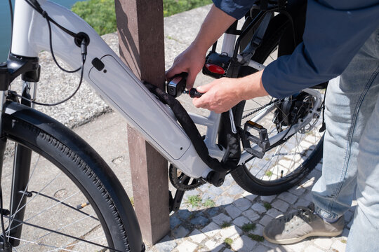 Young man in helmet securing his electric bicycle with a lock at a city bike rack near the water