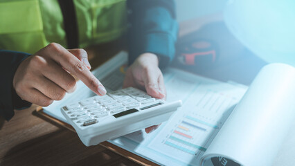 Cost estimation construction budget planning concept engineer hands using calculator analyzing financial report chart graph expense pricing audit working with hard hat tape measure on desk © HappyEva