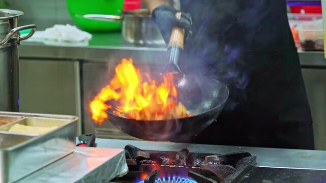 Chef stir fry busy cooking in kitchen.  Hands keep wok with fire. Closeup chef hands cook food with fire. Chinese cooking style. Man cooking fresh vegetables on pan. Chef cooking dish with flame 