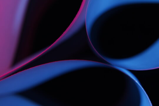 Papeles de oficina doblados en curvas fluidas, iluminados con luces multicolores en tonos azul, magenta y rojo sobre un fondo negro profundo. La escena es minimalista y futurista.