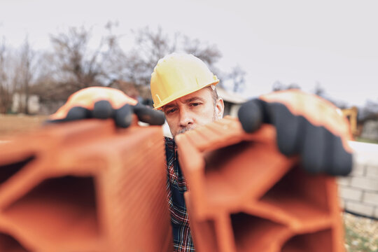 Bricklayer mason holding a regular brick outdoors on a construction site.
