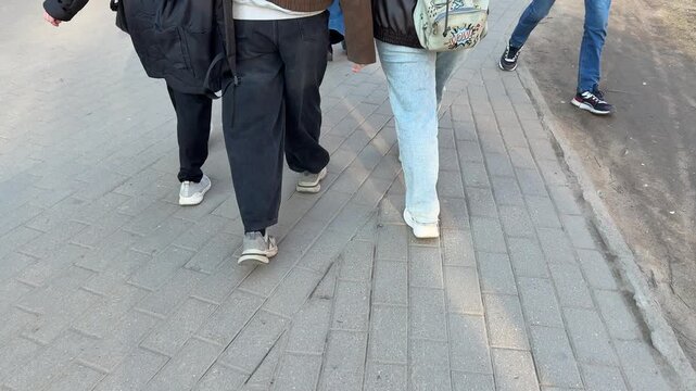 Female students walking footpath campus backpacks spring afternoon sun casting long shadows three friends in jackets and jeans