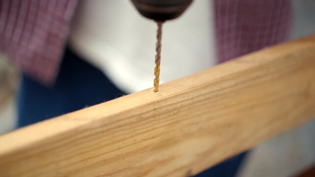 Confident carpenter man using cordless power drill to make hole in laminated wood board inside timber workshop. DIY woodworking, handmade furniture, home improvement and craftsmanship concept.