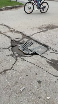 Large pothole on asphalt road covered with improvised metal plate, cracked pavement radiating fractures, shallow water pooling