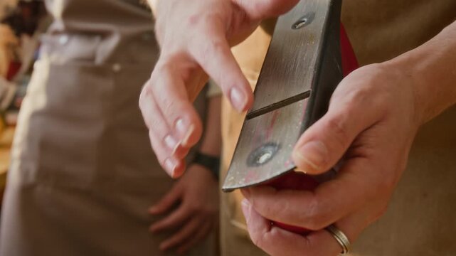 Close-up view of unrecognisable craftsman running fingers along blade of hand plane while instructing students on safety