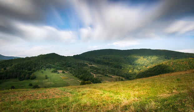 Rolling green hills and forest landscape under dramatic cloudy sky