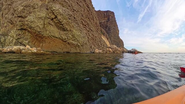 Kayaking paddle cliffs man navigates orange boat through calm sea water along steep rocky shoreline during peaceful summer adventure