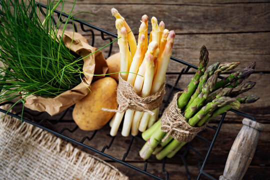 Fresh mixed asparagus with raw potatoes in a basket on rustic wood. Ingredients for a seasonal asparagus menu. Top view.