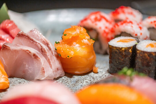 View of a fresh sushi and sashimi platter featuring salmon, white fish, and maki rolls with roe.