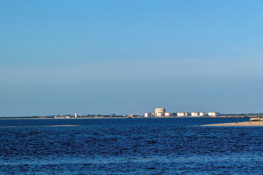 View of an industrial skyline with storage tanks and a checkered gasometer across the blue water under a clear sky in Barreiro, Setubal, Portugal.