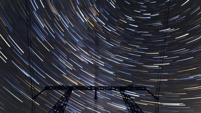 Vivid star trails swirling above pylon, long exposure timelapse capturing colorful streaks during Perseids, dynamic circular motion, rural electricity towers silhouette, dramatic night energy