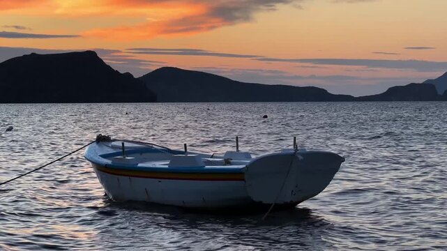 Small old boat at sunset on calm sea with mountains copy space