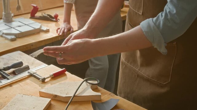 Anonymous craftsman grabbing piece of sandpaper from workbench and demonstrating it to unknown kids visiting his workshop for masterclass
