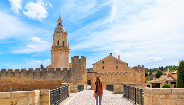 Traveler woman crossing bridge to medieval walls and cathedral tower in el burgo de osma, Soria province, Castile and Leon in spain