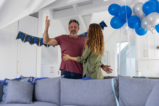 Couple celebrating behind gray sofa with blue ribbons, balloons and HAP banner near kitchen