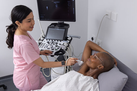 Diverse female patient and female sonographer performing ultrasound scan on exam bed with probe