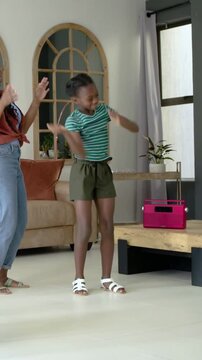 Vertical video: Dancing youth in green top doing quick steps at home to pink radio while mom copies
