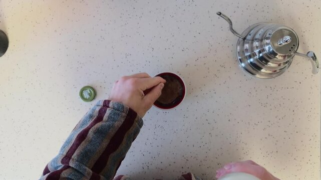 Unrecognizable Man Adding Fresh Milk from Bottle to Cup of Hot Coffee then Stirring with Spoon and Taking Mug Away Top Down View POV High Angle Shot on White Minimalist Table in Domestic Kitchen