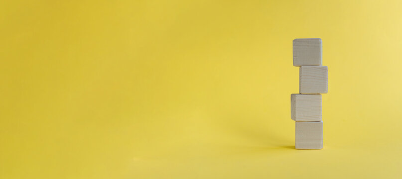 Four wooden blocks stacked on a bright yellow background. The blocks are plain and unmarked, creating a minimalist aesthetic.