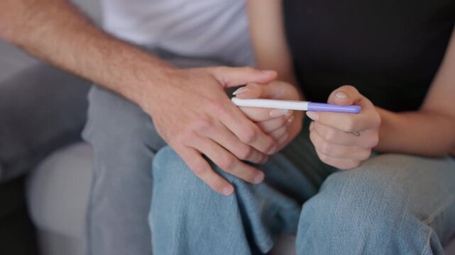 Close-up of a couple holding a pregnancy test kit together, expressing emotions related to pregnancy results, parenthood, fertility, family planning, and women&rsquo;s healthcare.