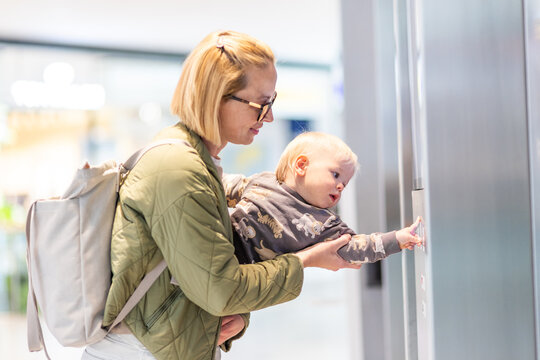 Mother holding a curious toddler as he presses an elevator call button in a modern building.